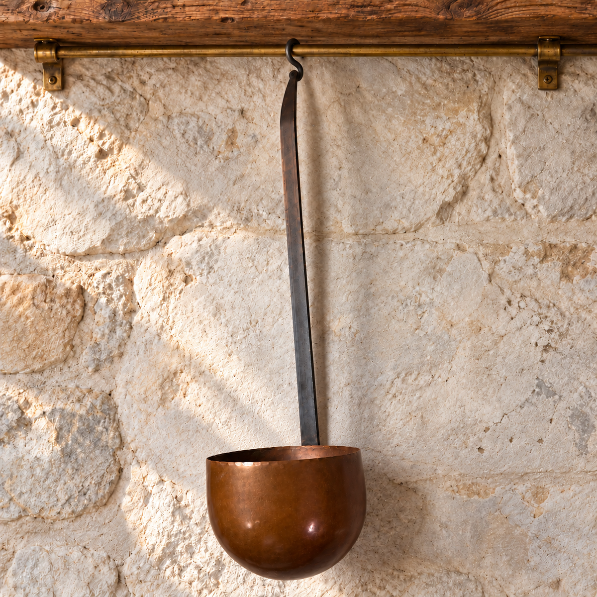 

French copper ladle with long iron handle hanging from an aged brass rail