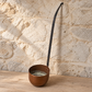 French copper ladle on a timber bench showing the deep bowl and curved iron handle