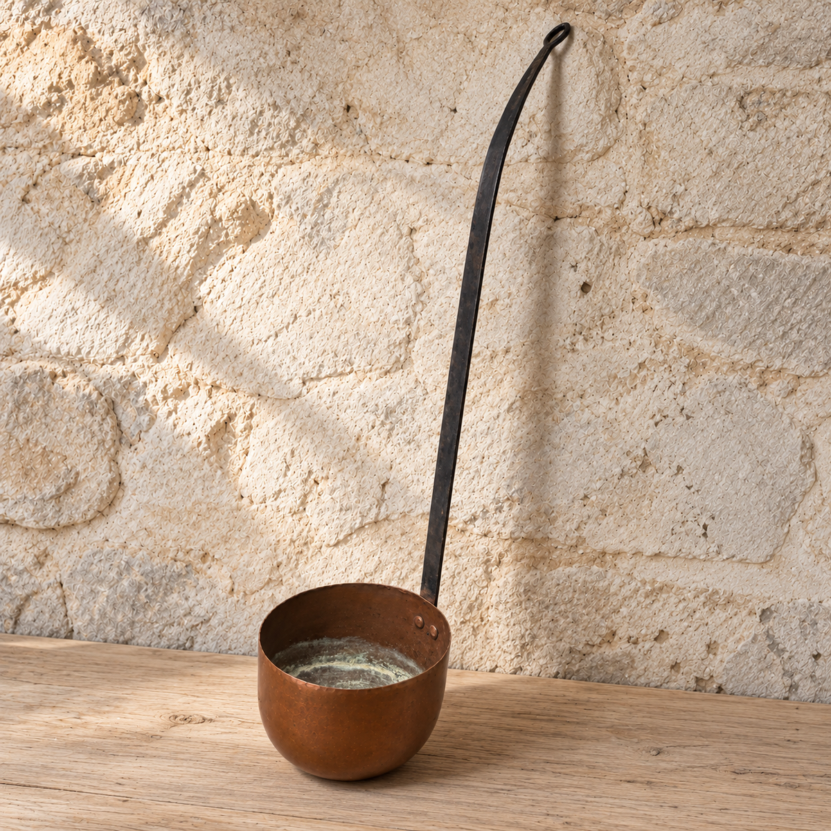 French copper ladle on a timber bench showing the deep bowl and curved iron handle