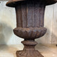 Decorative iron urn on a wooden surface with a neutral background. French antique urn. 