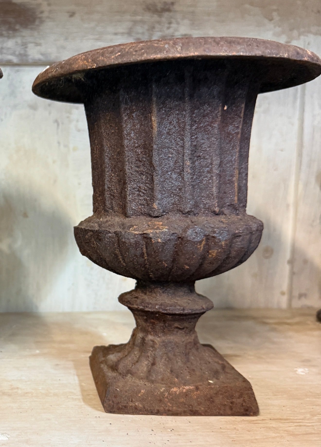 Decorative iron urn on a wooden surface with a neutral background. French antique urn. 