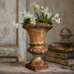 Rustic urn with white flowers on a wooden surface. French antique styling idea for urn. 