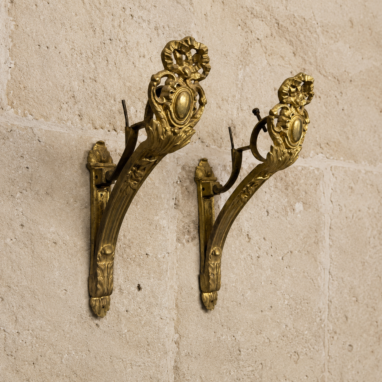 Pair of ornate brass French ANtique gilt curtain rod brackets wall brackets on a limestone stone wall.